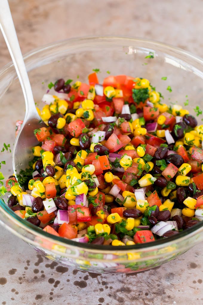 Corn, beans, tomatoes and seasonings mixed together in a glass bowl.