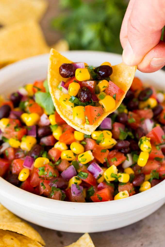 A hand holding a chip topped with black bean and corn salsa.