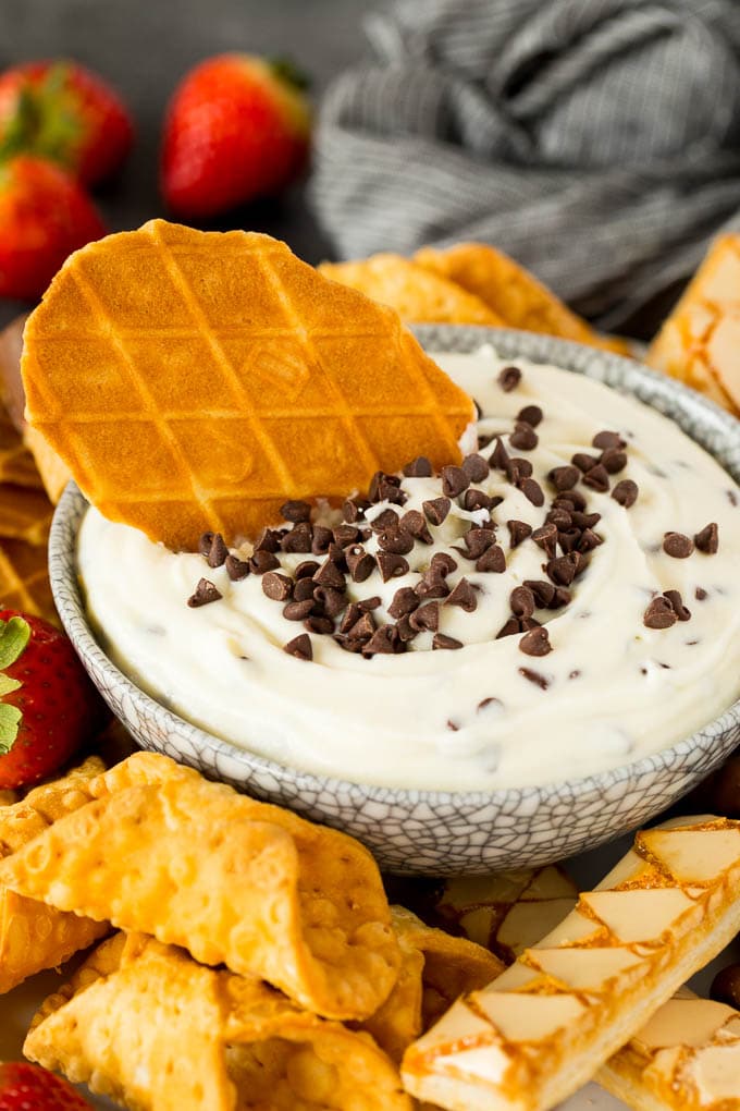 A bowl of cannoli dip with a waffle cookie in it.