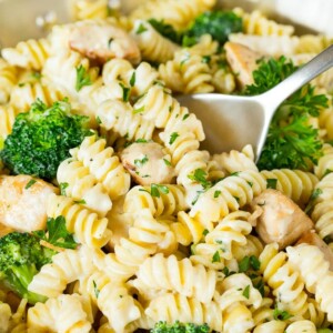 A pan of chicken broccoli Alfredo pasta with a serving spoon in it.