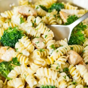 A pan of chicken broccoli Alfredo pasta with a serving spoon in it.