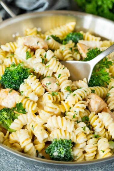 A pan of chicken broccoli Alfredo pasta with a serving spoon in it.