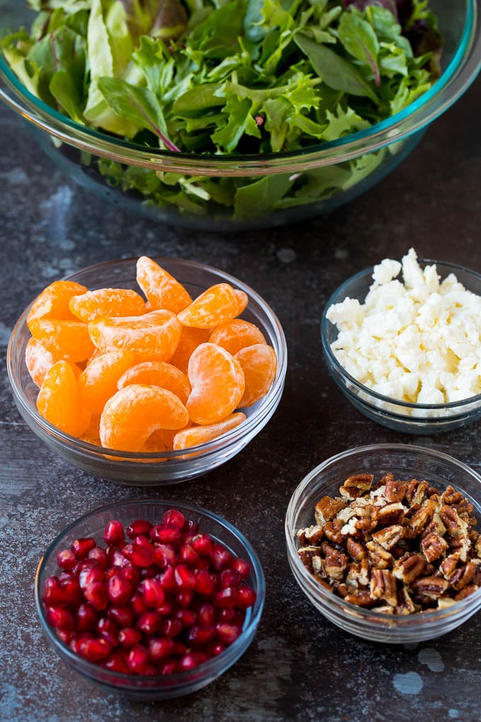 Bowls of lettuce, oranges, pomegranates, cheese and pecans.