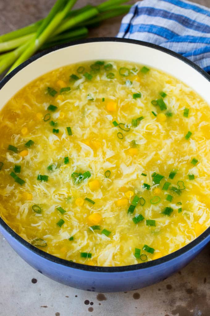 A pot of egg drop soup with corn and sliced green onions.