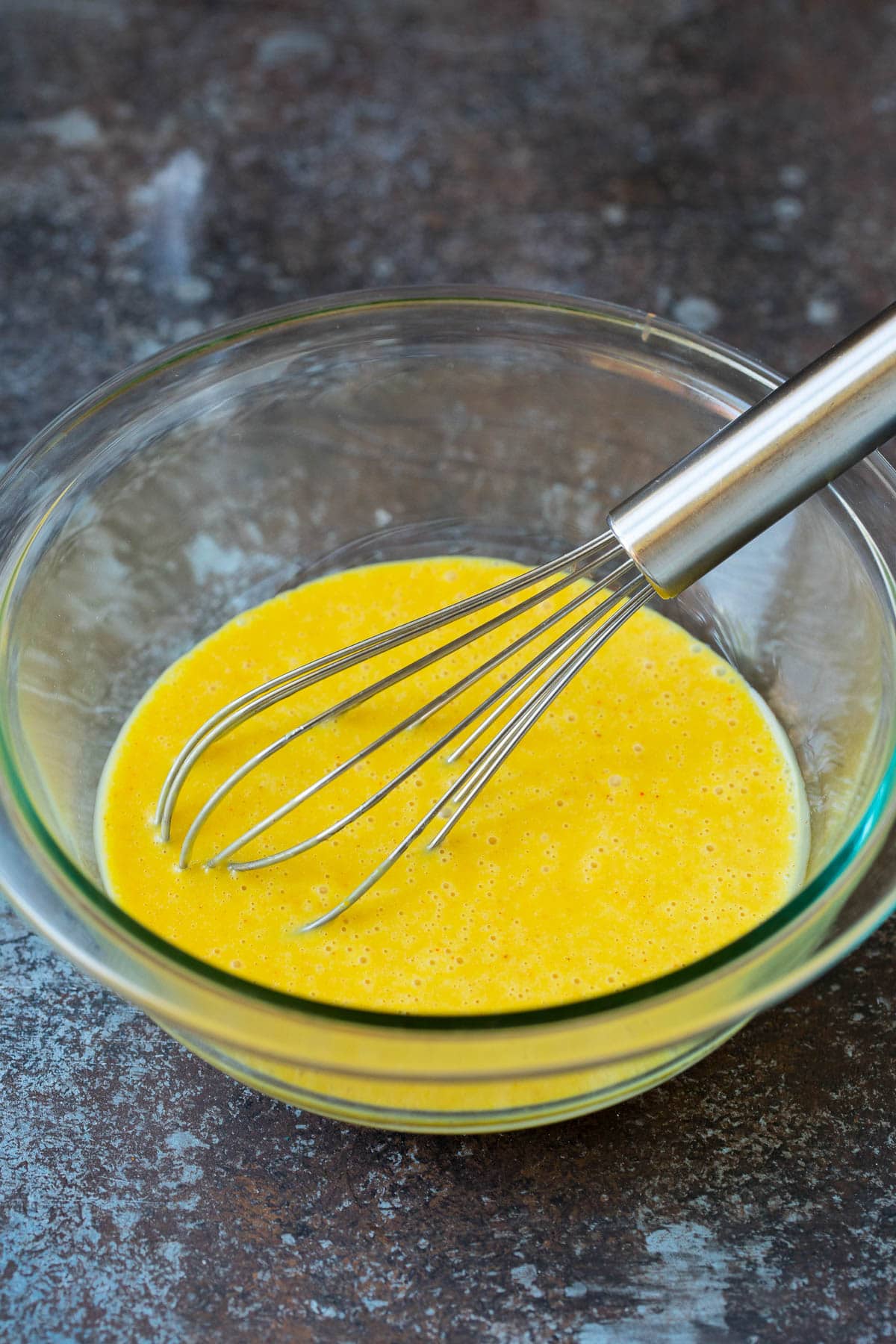 A whisk in a bowl of honey mustard.