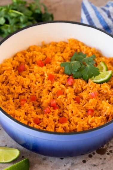 A pot of Mexican rice garnished with tomatoes, cilantro and lime wedges.