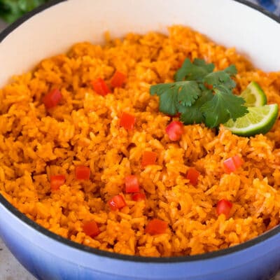 A pot of Mexican rice garnished with tomatoes, cilantro and lime wedges.