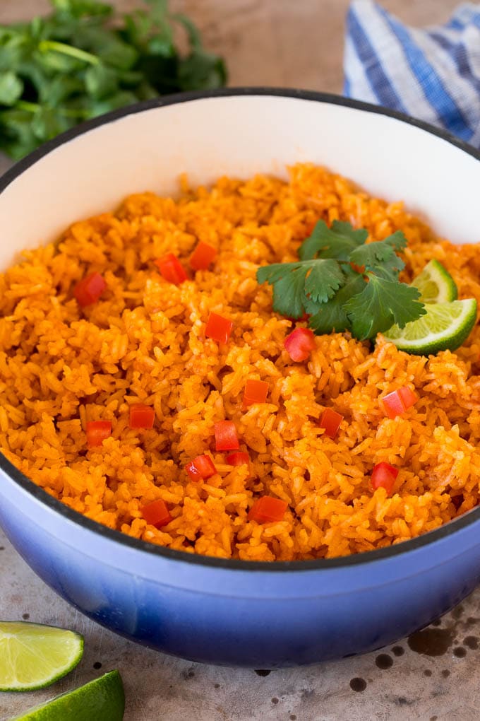 A pot of Mexican rice garnished with tomatoes, cilantro and lime wedges.