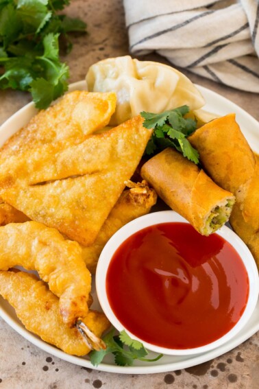 A bowl of sweet and sour sauce served with egg rolls, shrimp and wontons.