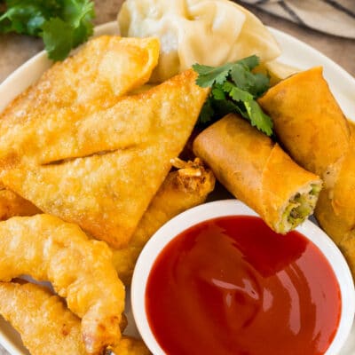 A bowl of sweet and sour sauce served with egg rolls, shrimp and wontons.