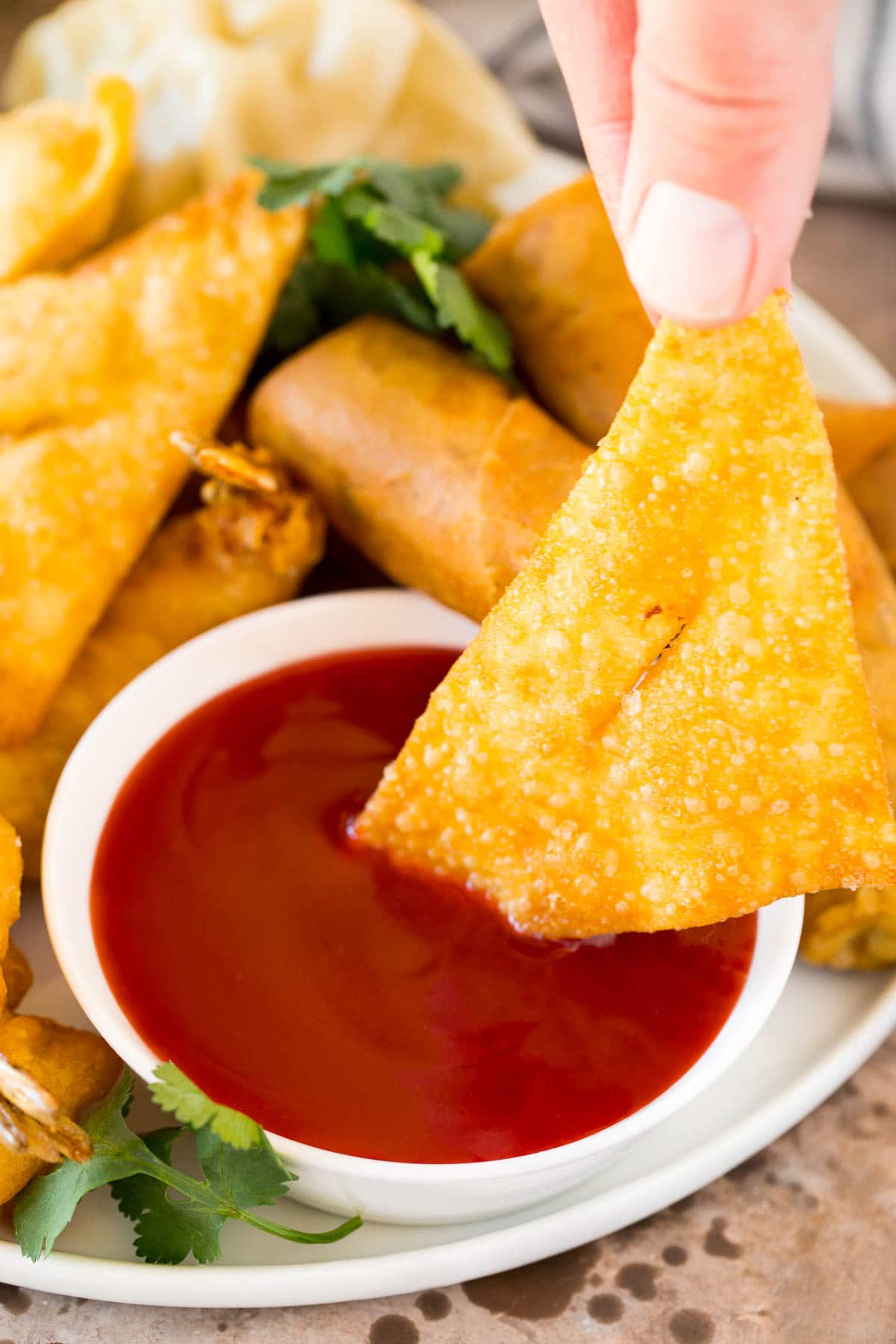 A wonton being dipped into a bowl of sweet and sour sauce.