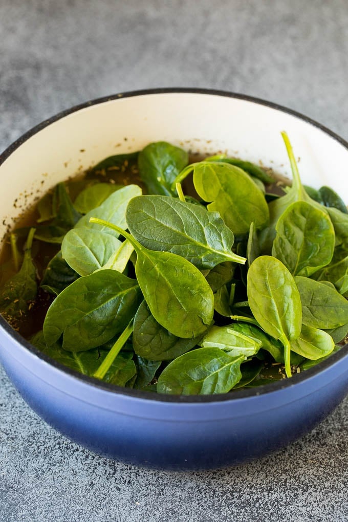 A pot of soup with fresh spinach in it.