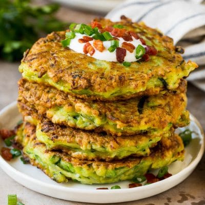 A stack of zucchini fritters topped with sour cream and bacon.