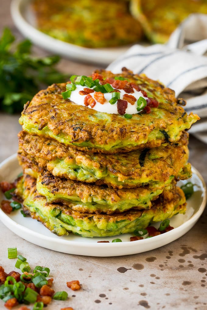 A stack of zucchini fritters topped with sour cream and bacon.