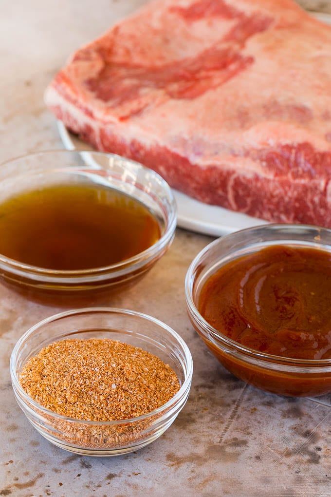 Raw brisket with bowls of beef broth, sauce and seasoning.