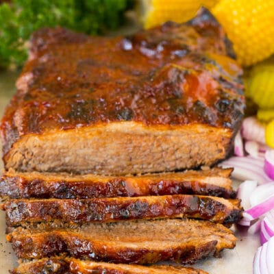 Instant Pot brisket on a tray with red onions and corn on the cob.