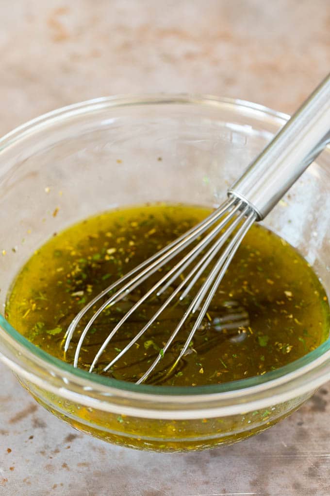 A whisk in a bowl of salad dressing.