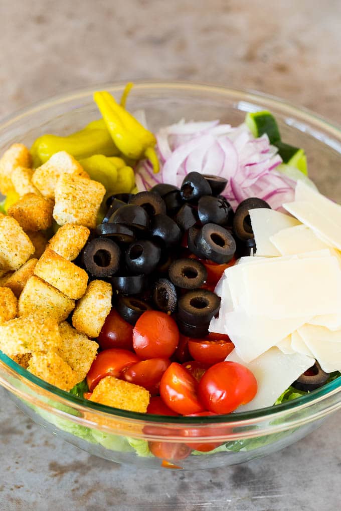 A bowl of lettuce topped with olives, tomatoes, cheese and croutons.