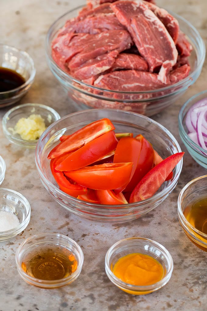 Bowls of ingredients including onions, tomatoes, sliced beef and seasonings.