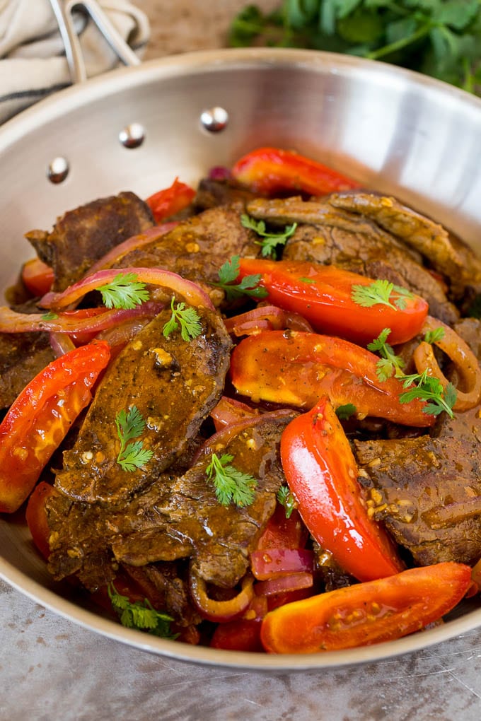 A pan of lomo saltado with beef, tomatoes, onions and cilantro.