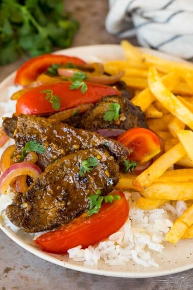 A plate of lomo saltado served with rice and french fries.
