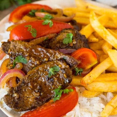 A plate of lomo saltado served with rice and french fries.