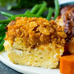 A portion of noodle kugel on a plate served with chicken and vegetables.