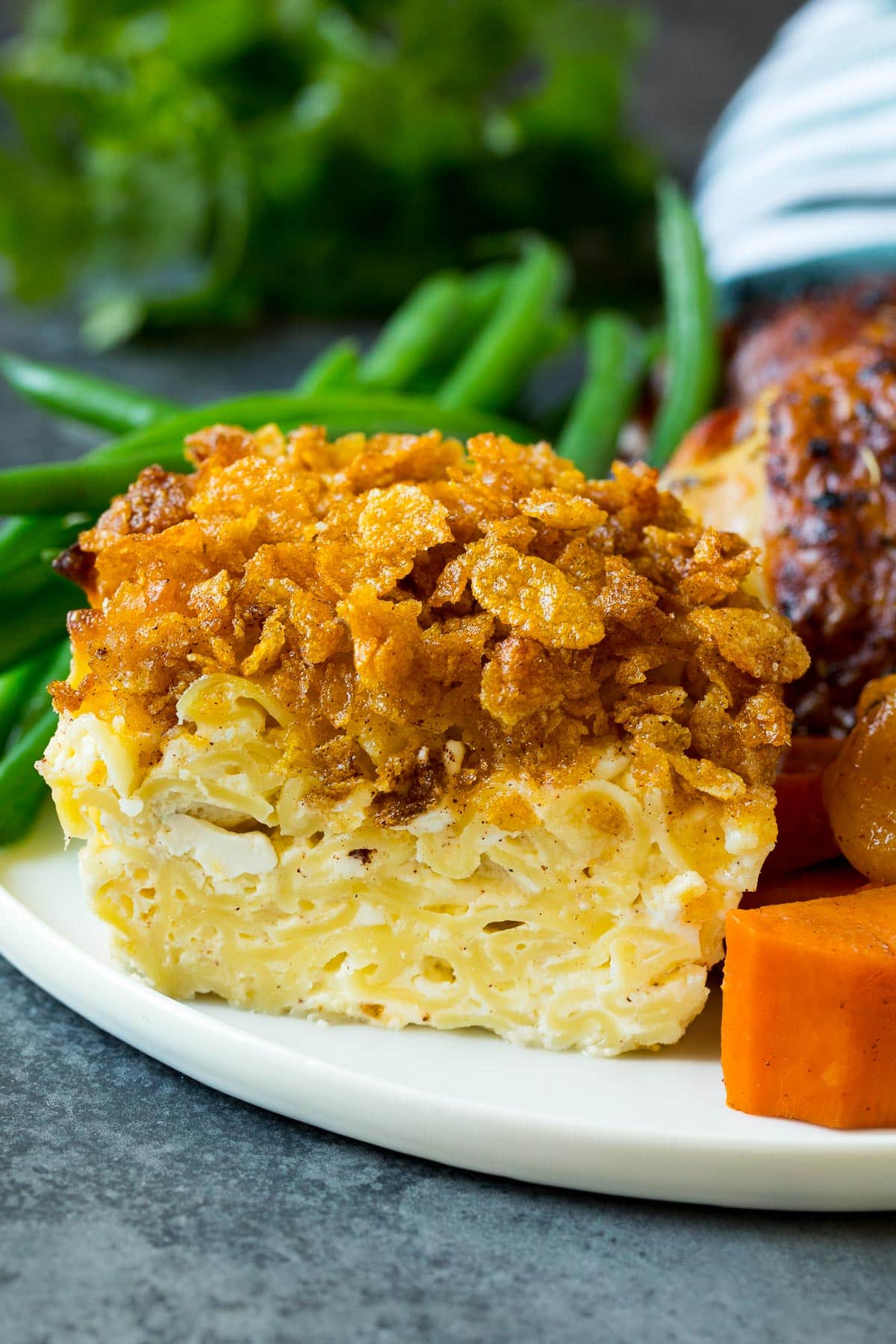 A portion of noodle kugel on a plate served with chicken and vegetables.