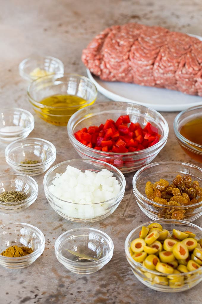 Bowls of ingredients including vegetables, spices, olives and raisins.