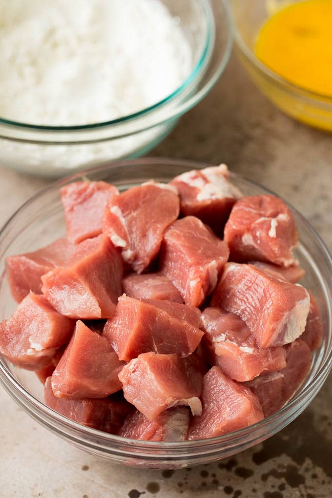 Cubes of pork tenderloin, a bowl of flour and a bowl of eggs.