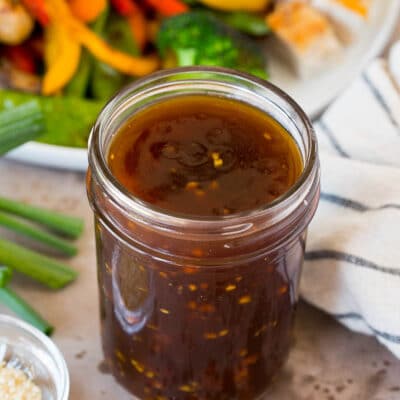 A jar of teriyaki sauce shown next to a plate of vegetables and chicken.