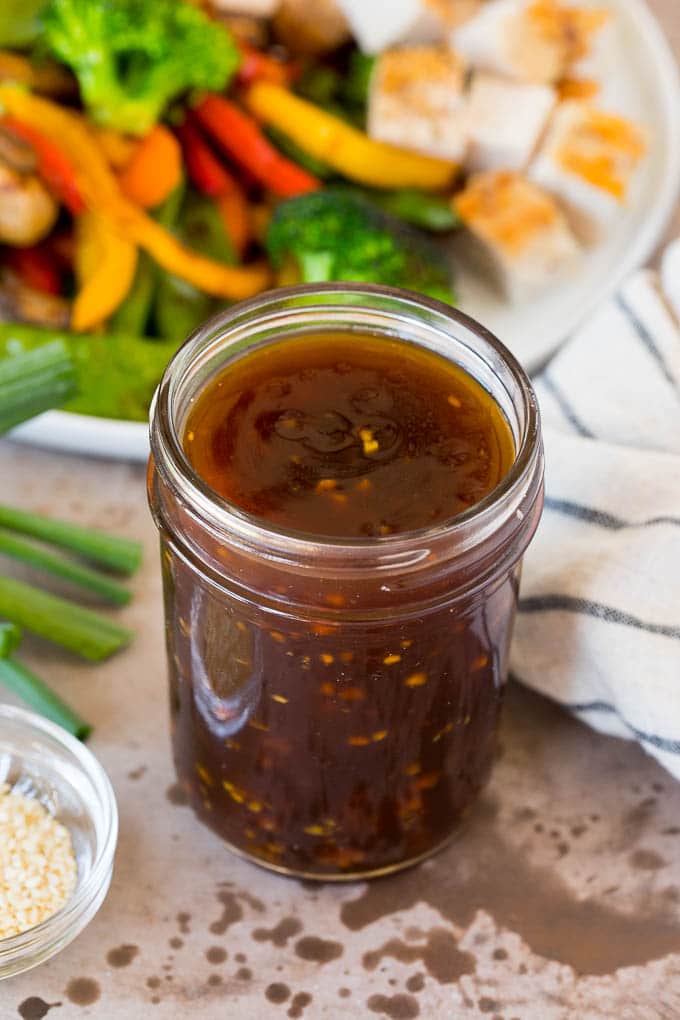 A jar of teriyaki sauce shown next to a plate of vegetables and chicken.