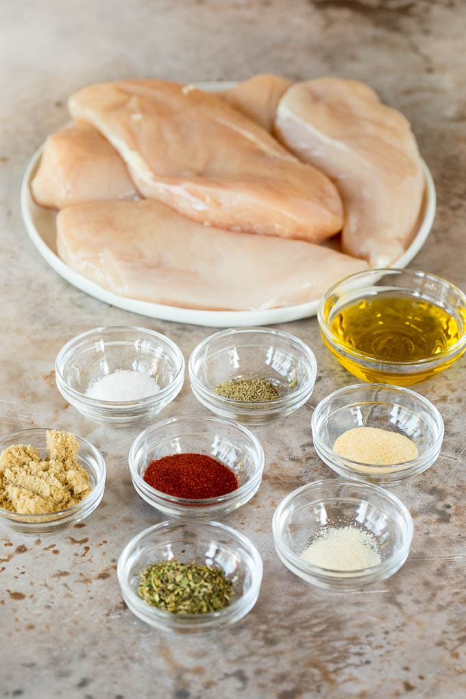 Chicken on a plate with bowls of herbs and spices.