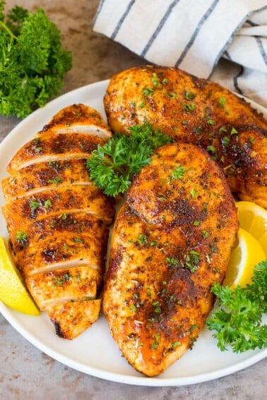 Air fryer chicken breast on a plate with lemon and parsley for garnish.