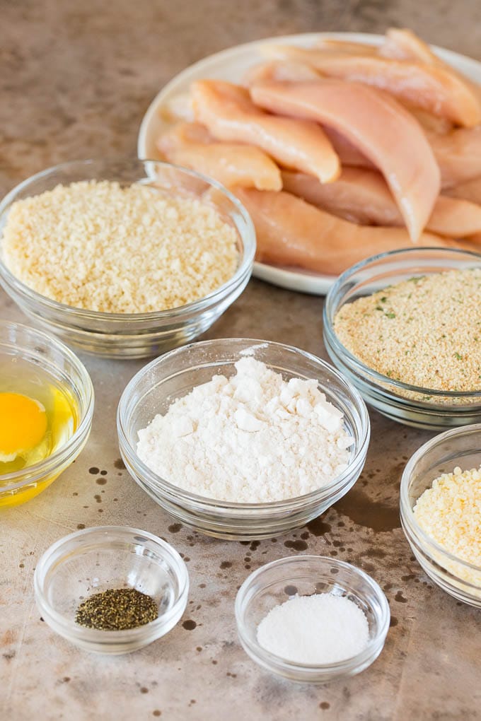 Bowls of flour, eggs, breadcrumbs and seasonings and a plate of chicken.
