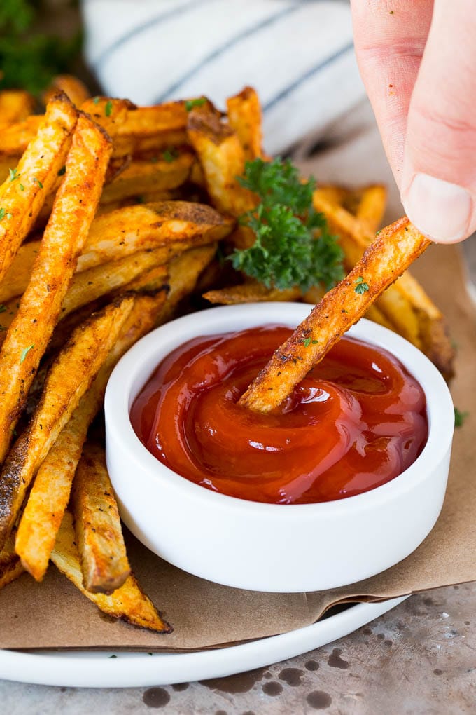 A hand dipping air fryer french fries into ketchup.