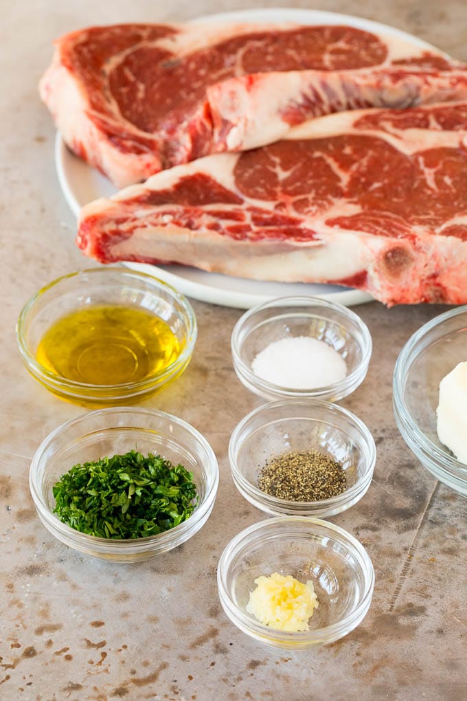 A plate of steak with bowls of garlic, butter and herbs.