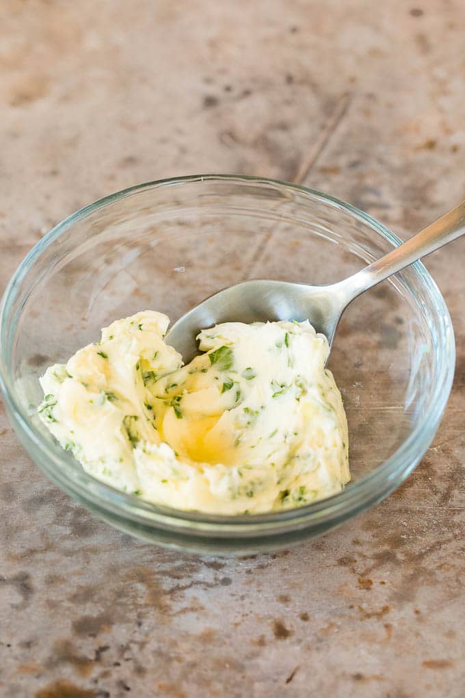 A bowl of garlic and herb butter with a spoon in it.