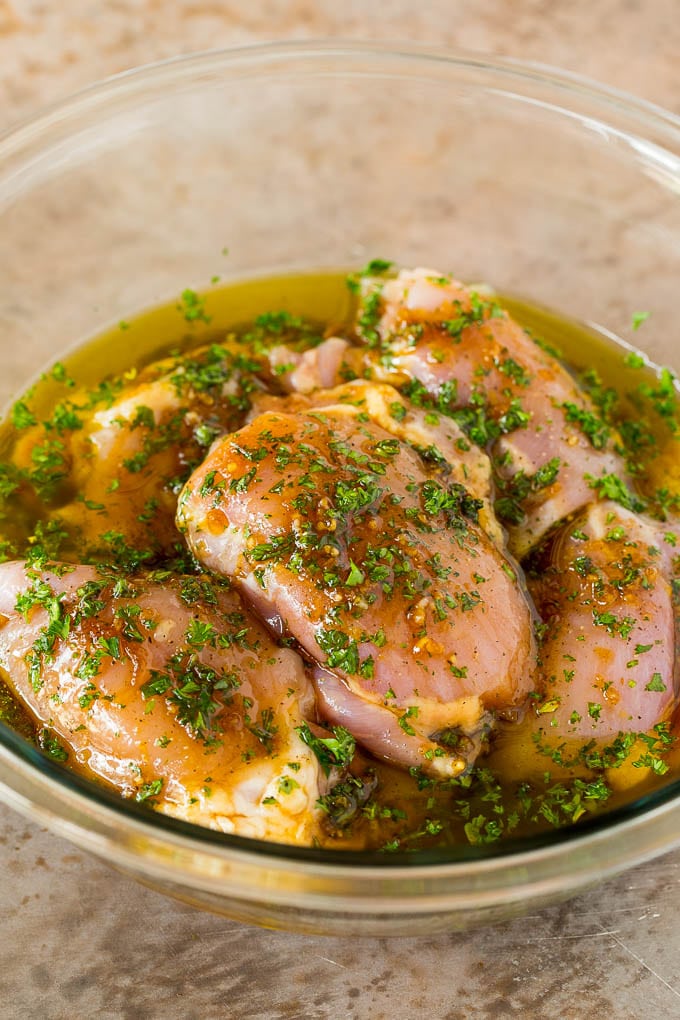 Raw chicken thighs in a bowl of marinade.