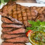 Sliced churrasco served with a bowl of chimichurri sauce.