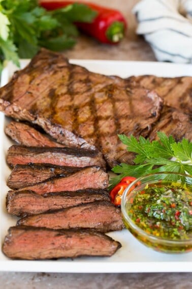 Sliced churrasco served with a bowl of chimichurri sauce.