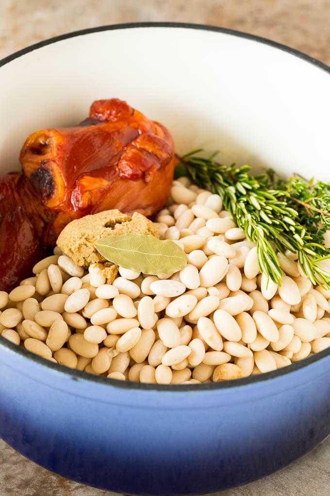 Beans in a pot with a ham hock and herbs.