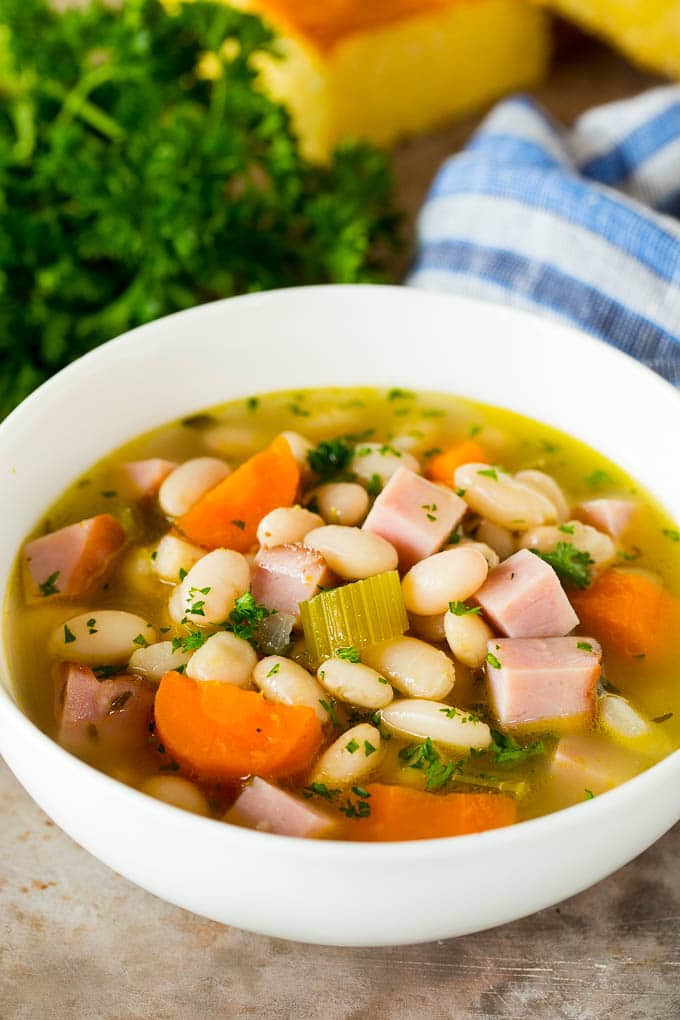 A bowl of ham and beans in broth with carrots and celery.