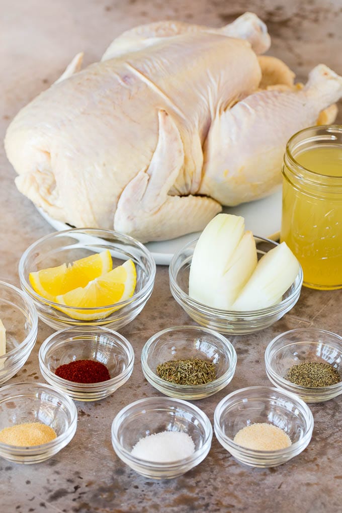 Bowls of spices and seasonings and a raw chicken on a plate.