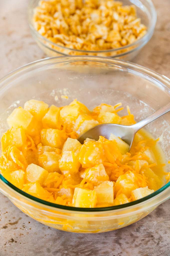 A bowl of pineapple chunks mixed with cheddar cheese, flour and sugar.