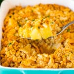 A spoon holding a serving of pineapple casserole topped with crackers and parsley.