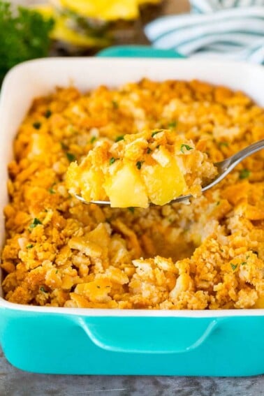 A spoon holding a serving of pineapple casserole topped with crackers and parsley.