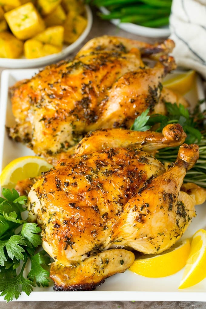 Roasted cornish hen on a serving tray garnished with herbs and lemon.
