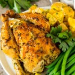 Roasted cornish hen on a plate served with potatoes and green beans.