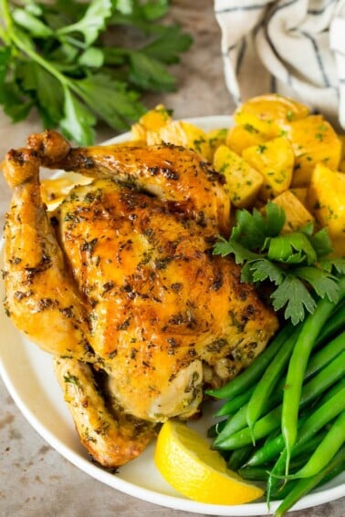 Roasted cornish hen on a plate served with potatoes and green beans.